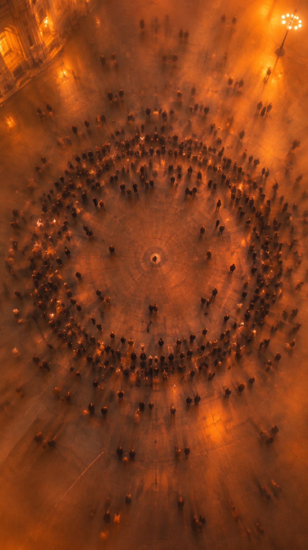A crowd seen from above standing in a ring on a square in orange haze